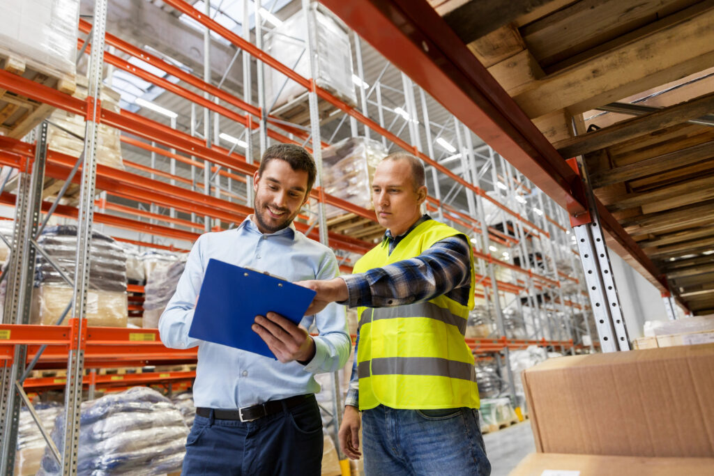 Image of employee with a clipboard having a conversation with another employee inside a warehouse.