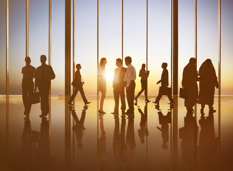 Diverse business professionals networking and collaborating in a modern office during sunset, representing talent acquisition, workforce strategy, and hiring optimization.