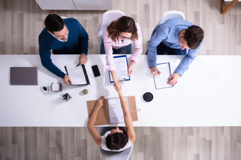 Overhead view of four people reviewing documents across an office table, with two shaking hands.
