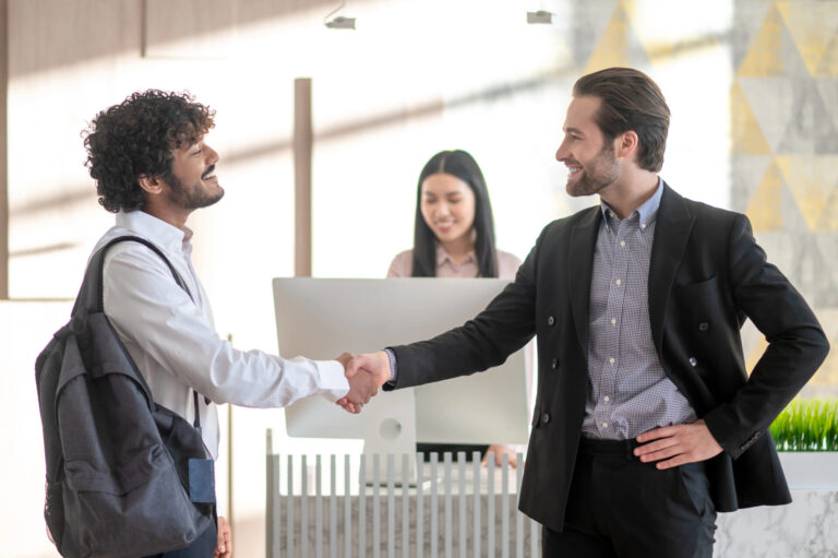 Two men shaking hands at an office reception desk.