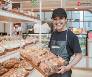 Hispanic male bakery worker adding pastries to a display case.