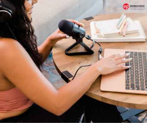 Female influencer speaking into a podcasting mic while typing on a laptop