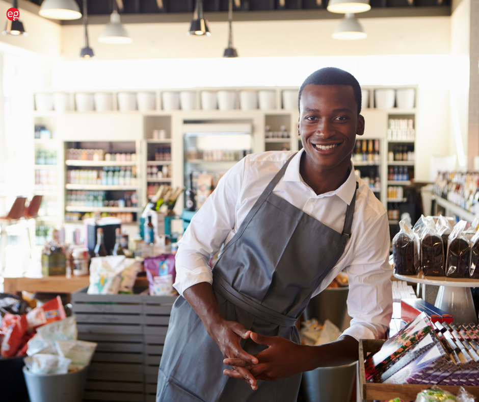 Black man in an apron leaning on a store shelf