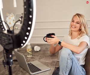 Woman recording on a phone with a ring light holding a cup of coffee