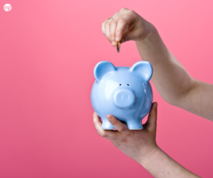 Blue piggy bank against a pink background with hands adding coins to the piggy bank
